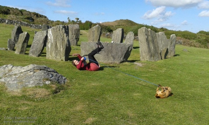 woman and dog gleefully rolling in the grass at Drombeg Stone Circle